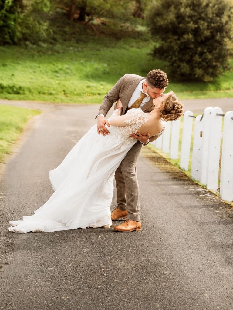 Bride and groom sharing a dip kiss on a garden path
