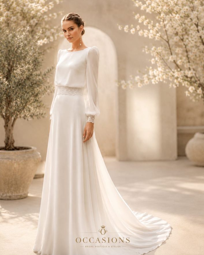 Bride in a long-sleeved lace gown in a sunlit courtyard with blossoms