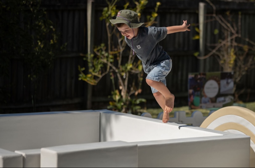 Boy mid-air jumping into a white soft play ball pit