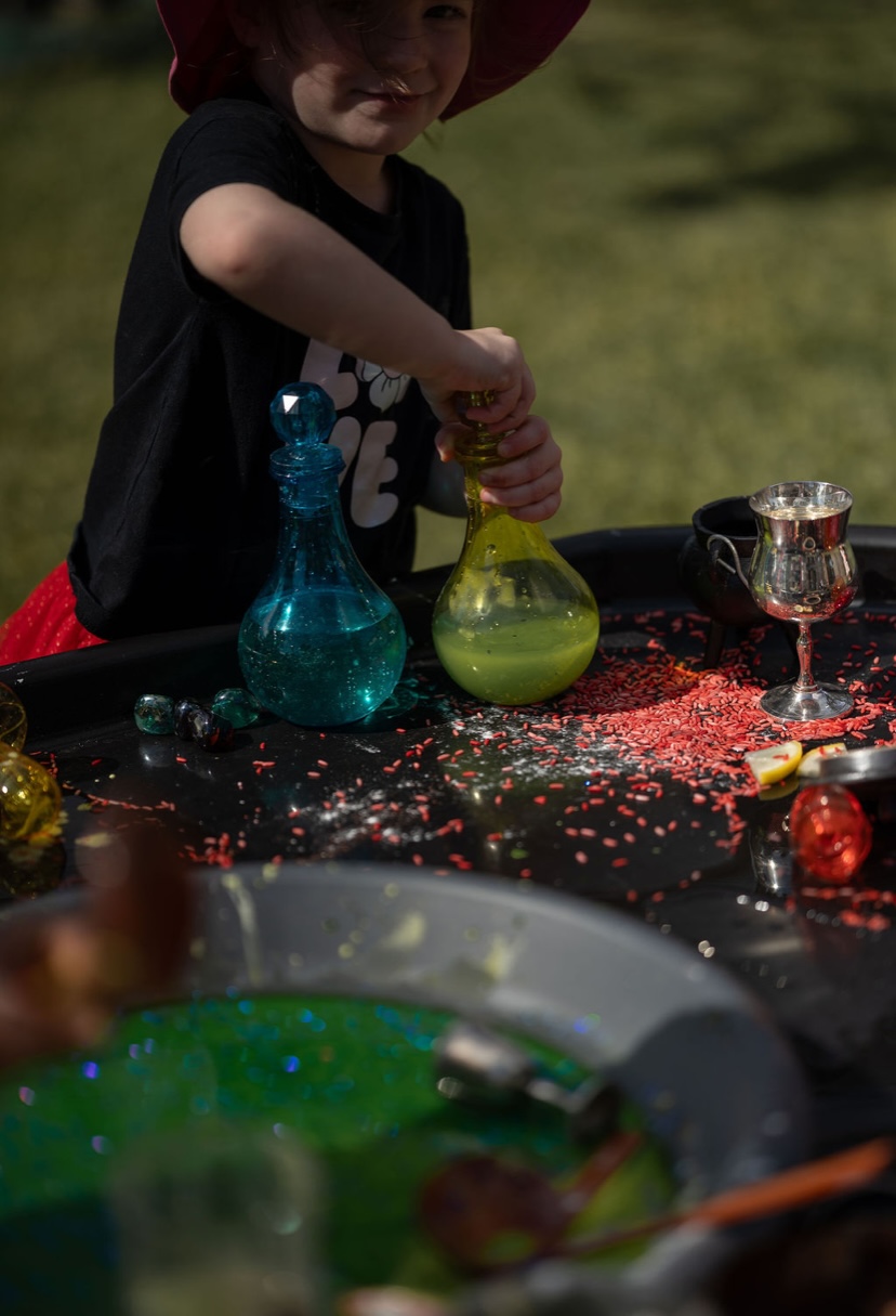 Child pouring green liquid into a cauldron sensory play