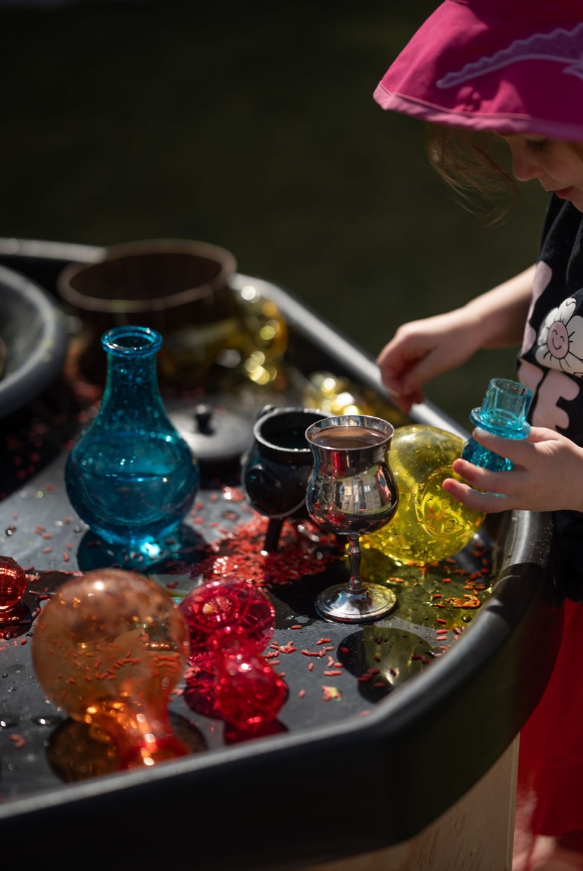 Child reaching for a turquoise bottle on a sensory tray