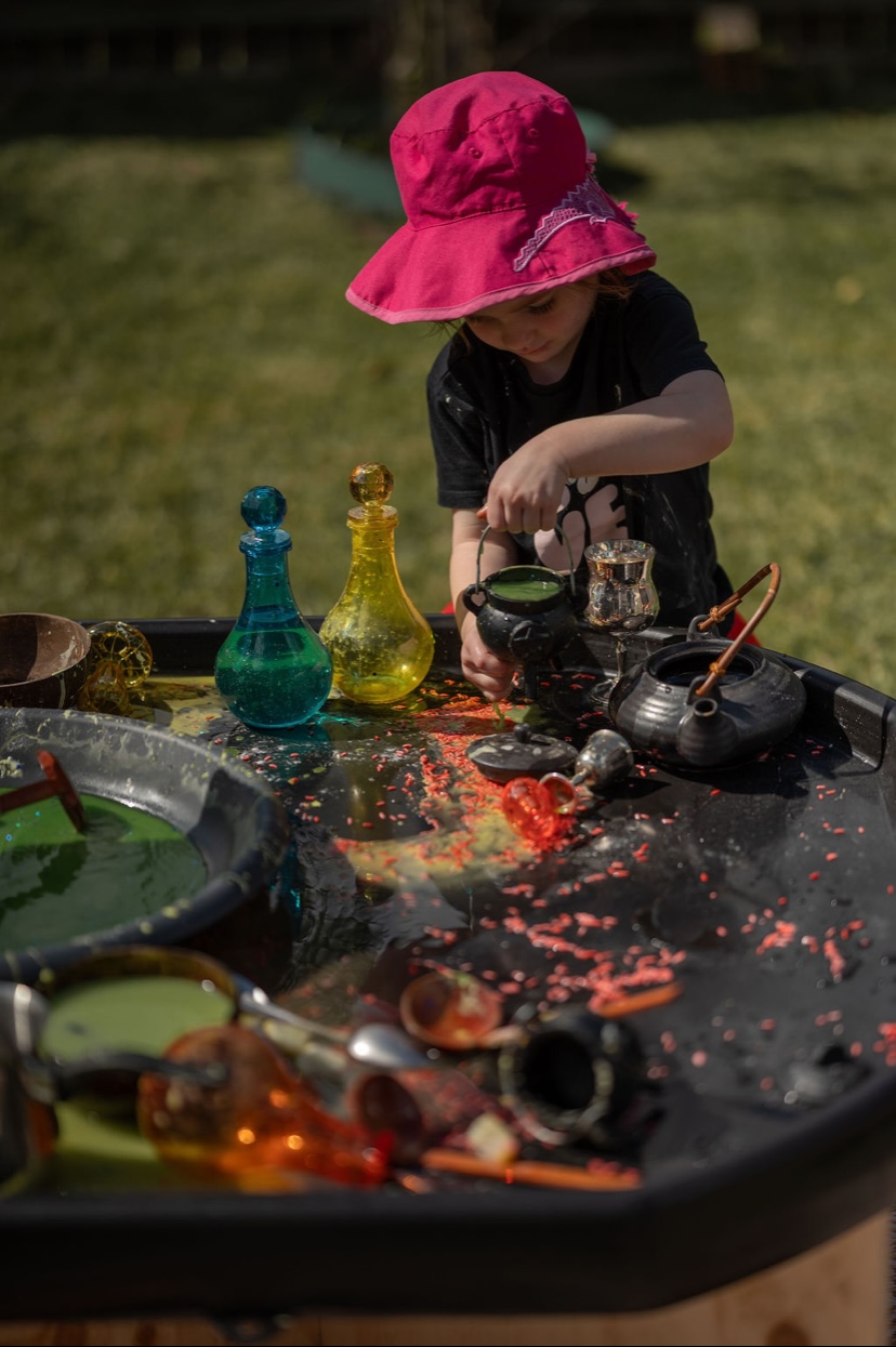 Child playing with potion bottles at a tuff tray