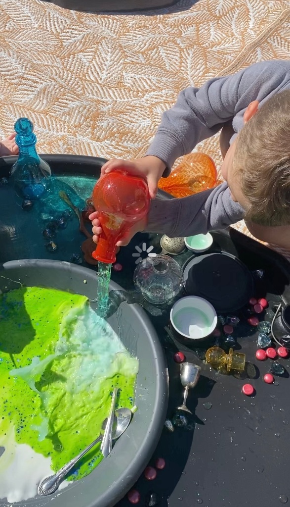 Child pouring green potion into a sensory bin