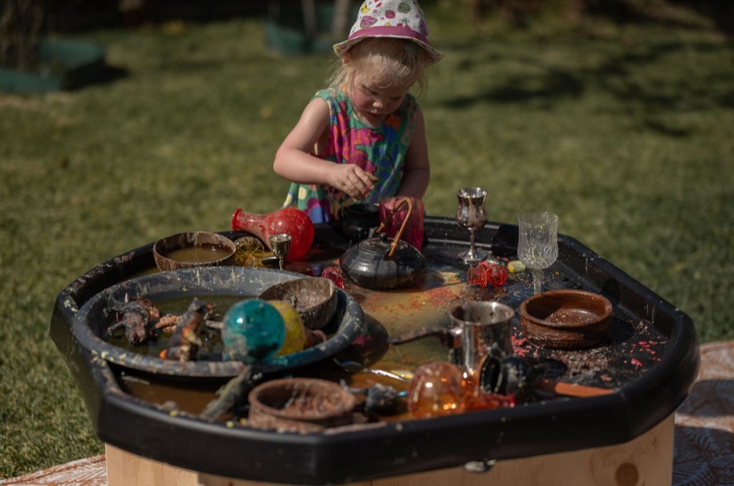 Child playing potion making at a black tuff tray
