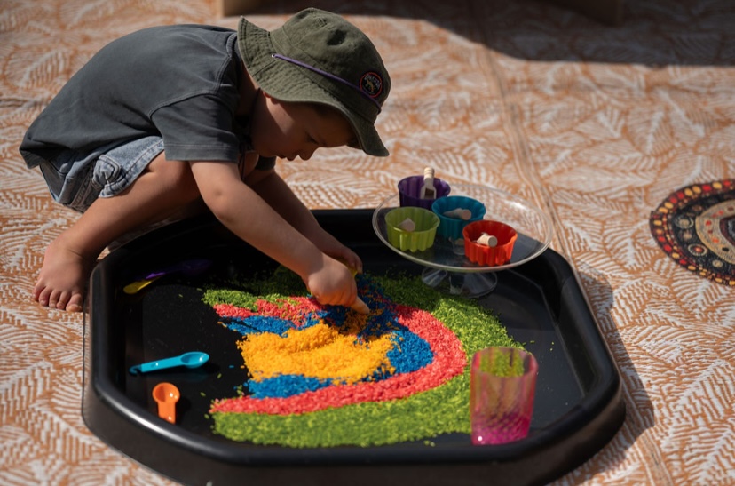 Child arranging rainbow dyed rice on a tuff tray