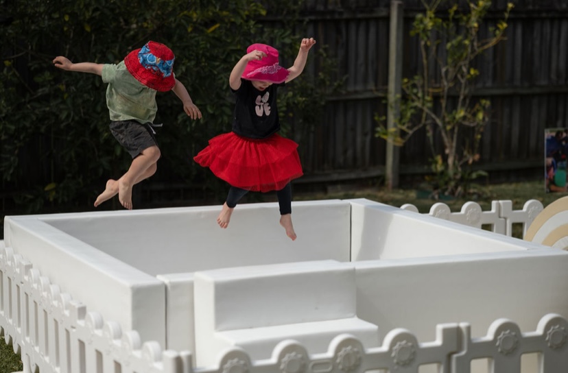 Two children jumping into a white ball pit