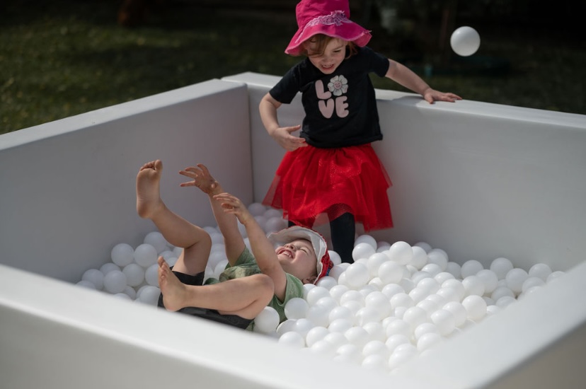 Children laughing and playing in a white ball pit