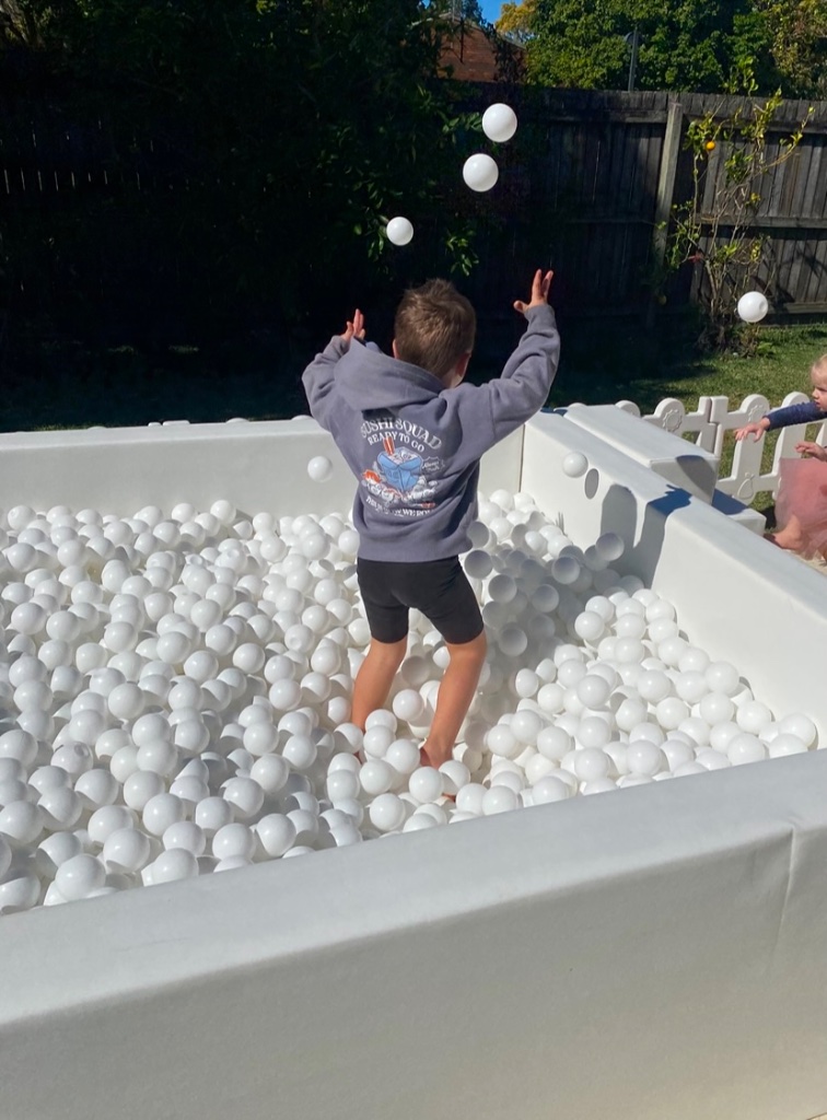 Child playing in a white ball pit tossing balls in the air
