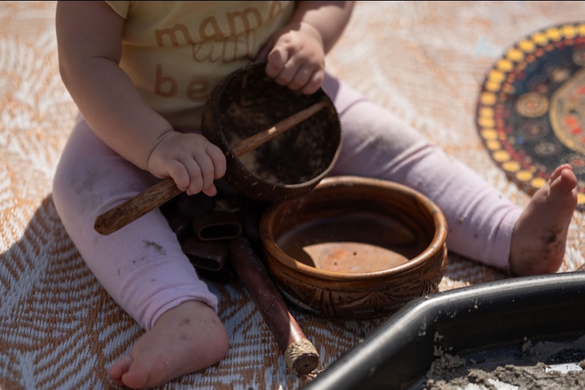 Baby holding a coconut shell bowl during sensory play