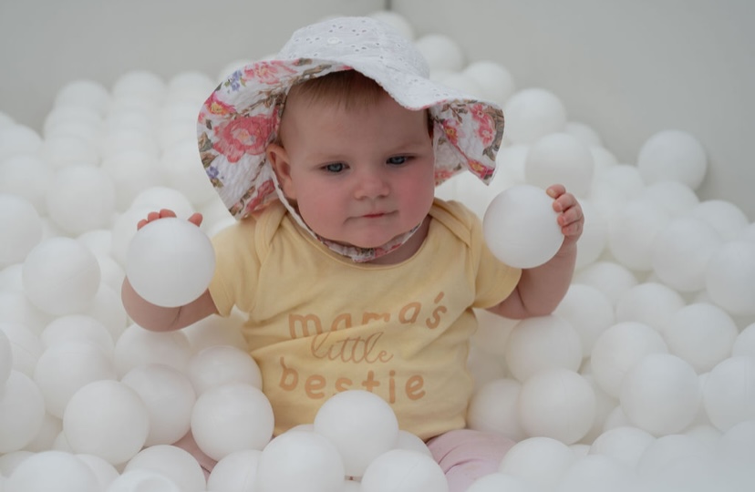Toddler sitting in a white ball pit holding balls