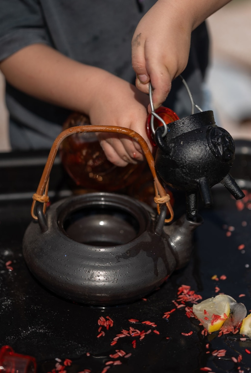 Child pouring red rice into a teapot sensory play