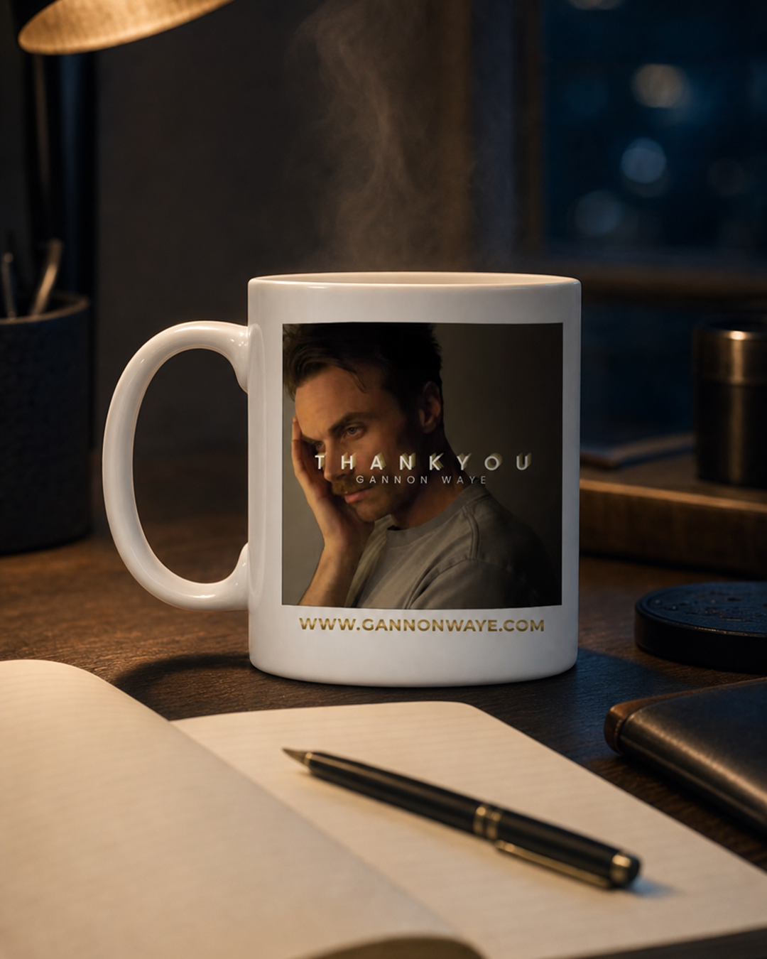 Gannon Waye mug beside an open cream notebook and pen on a dark timber table, with warm steam rising. The mug carries the Respect Is Earned campaign artwork.