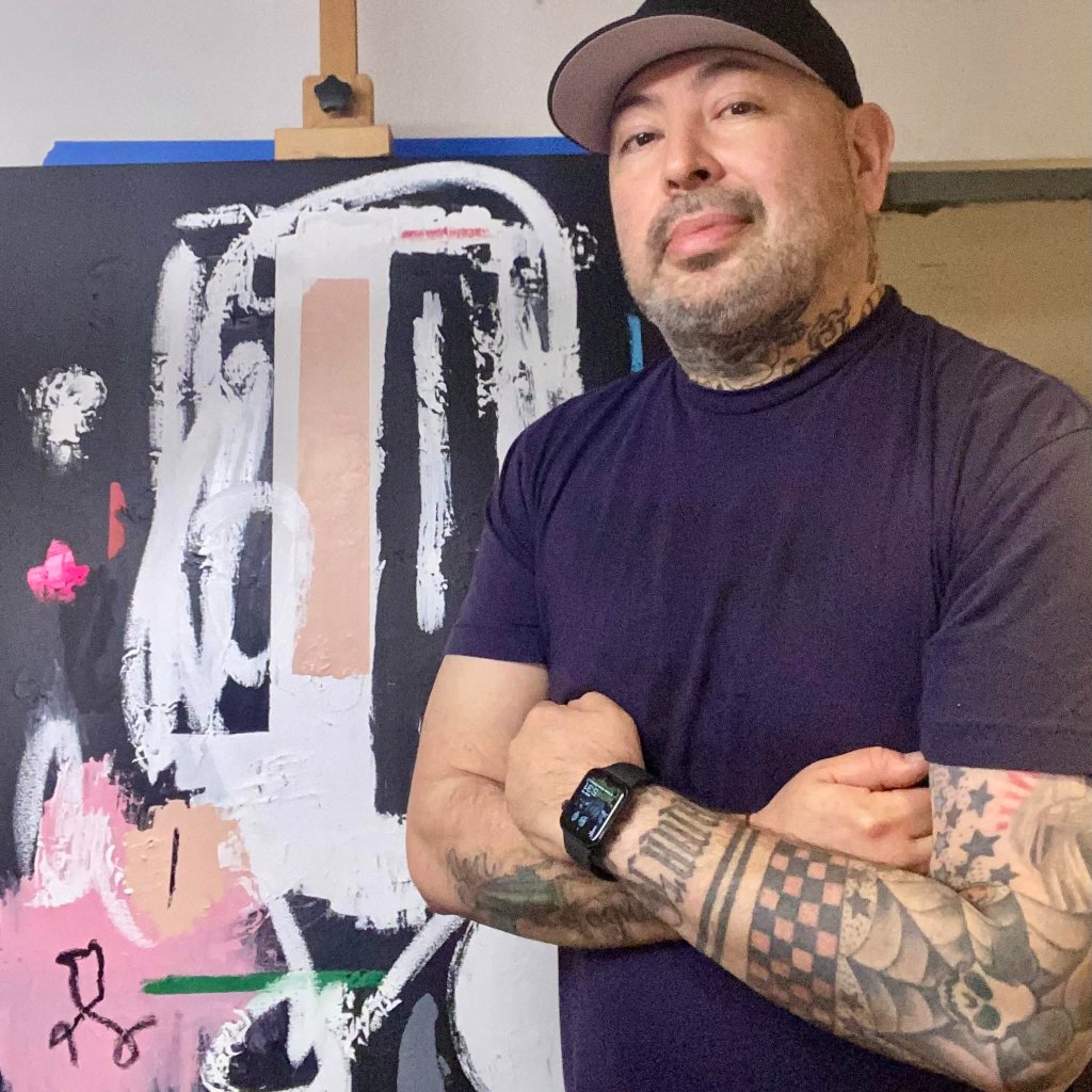Artist Anouk Rawkson standing with arms crossed beside a large abstract painting in his studio.