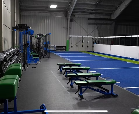 wide view of the Big Cat Twinsburg strength training area with green and blue equipment, benches, and a blue turf track