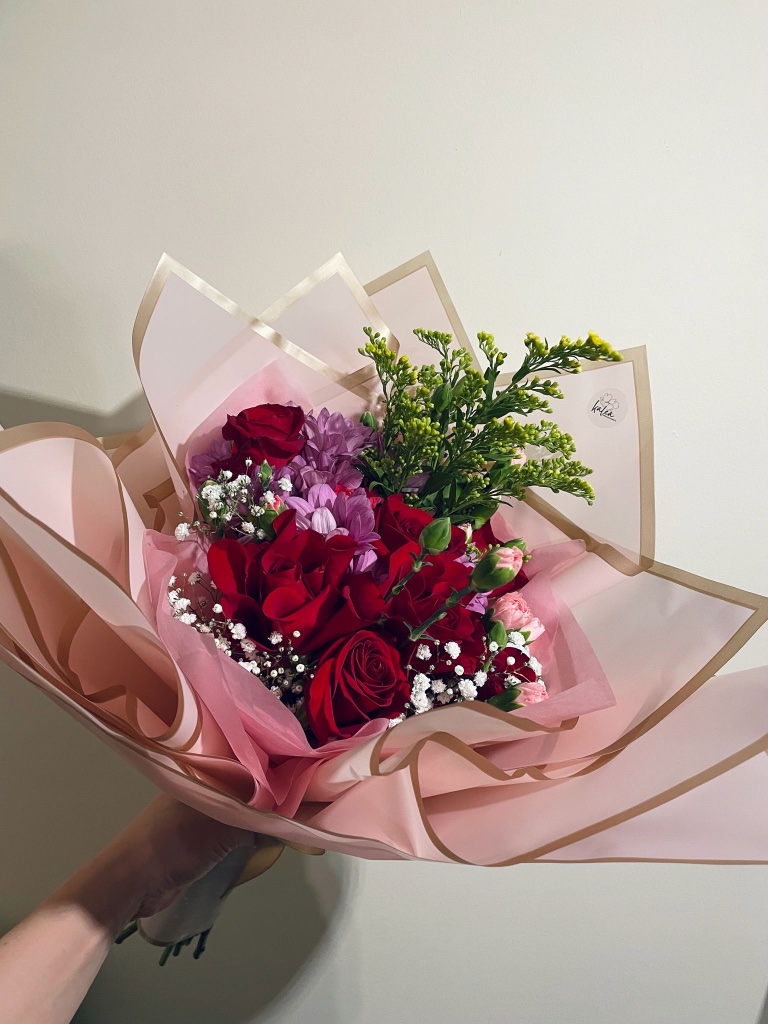 Red roses and mixed blooms wrapped in blush paper by Kalea Arrangements
