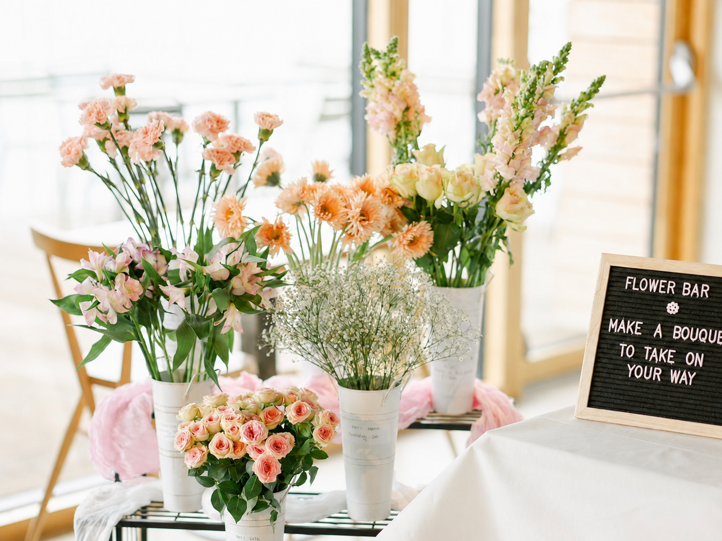 Flower bar display with seasonal flowers in white vases and a sign reading Make a Bouquet to Take on Your Way