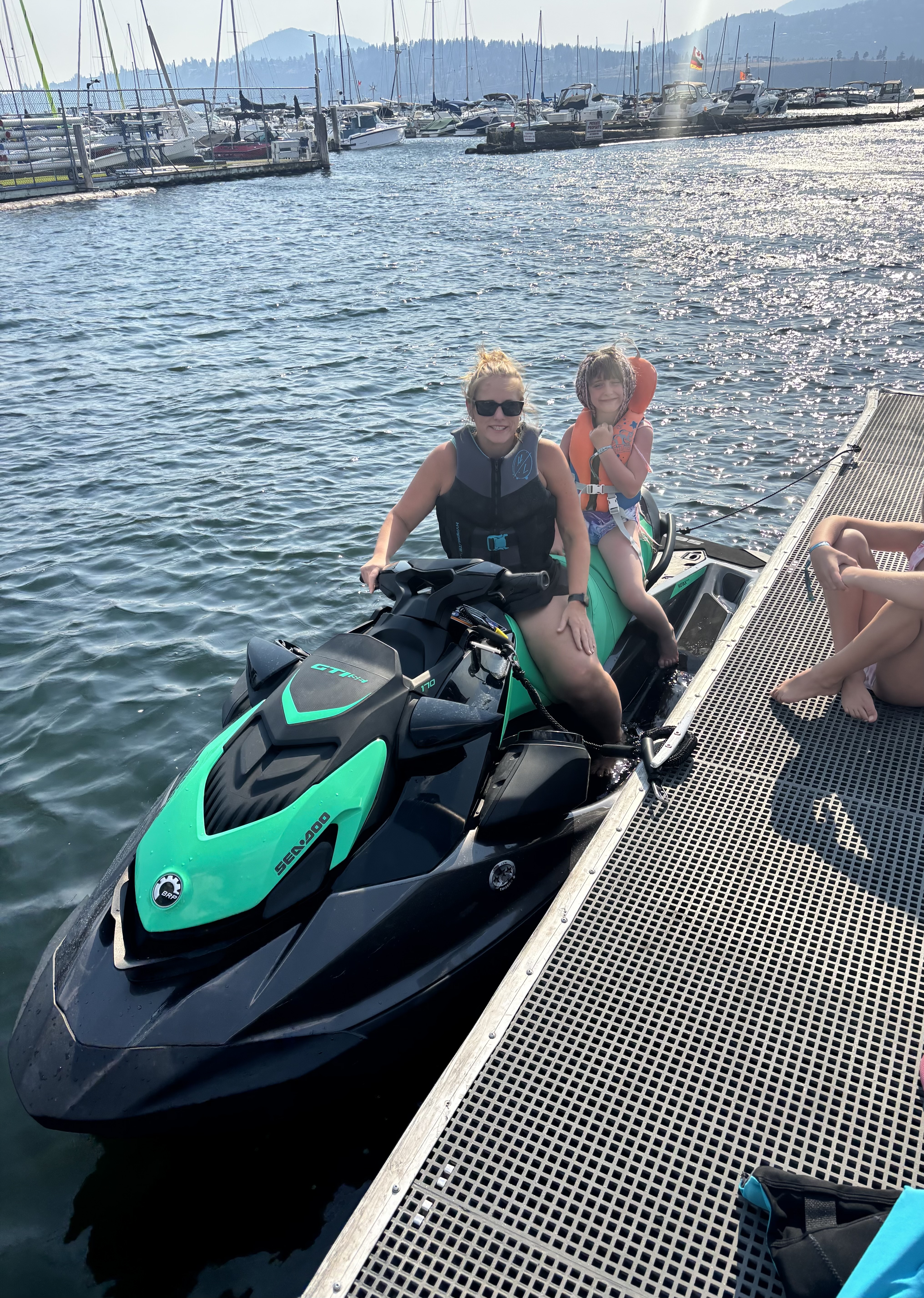 A mother and young girl smiling together on a Sea-Doo at the dock