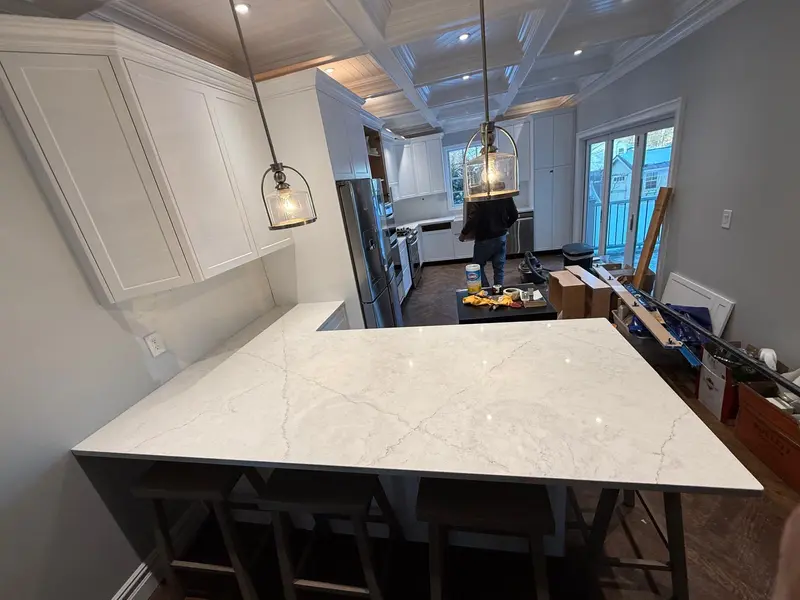 Completed white quartz L-shaped island with white shaker cabinets, coffered ceiling and pendant lights, Schenectady