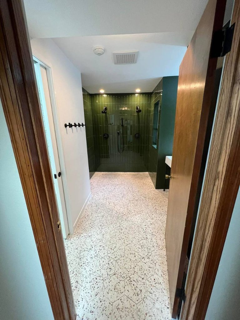 Full room view — forest green zellige, terrazzo hex floor, double shower, console sink
