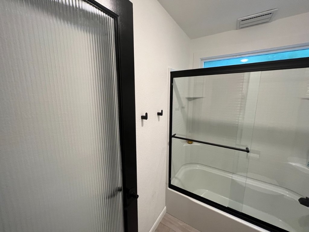 Tub/shower combo with matte black fixtures and reeded glass sliding door
