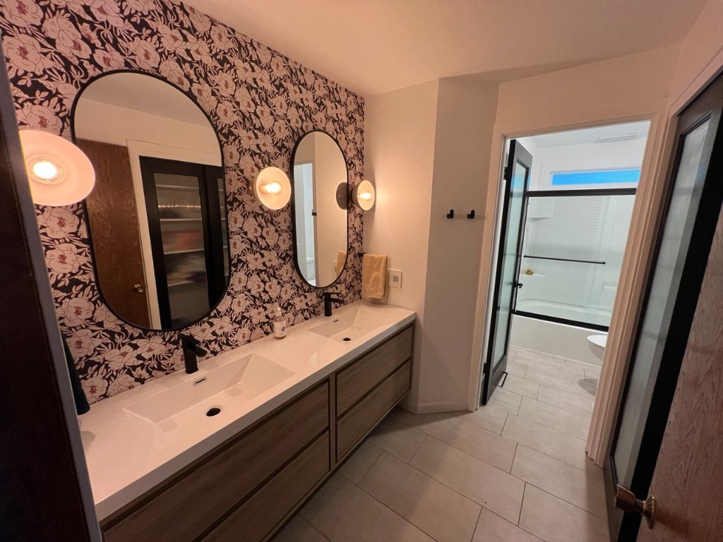 Full girls bathroom — dual vanity, floral wallpaper, reeded glass shower door, globe sconces, matte black throughout