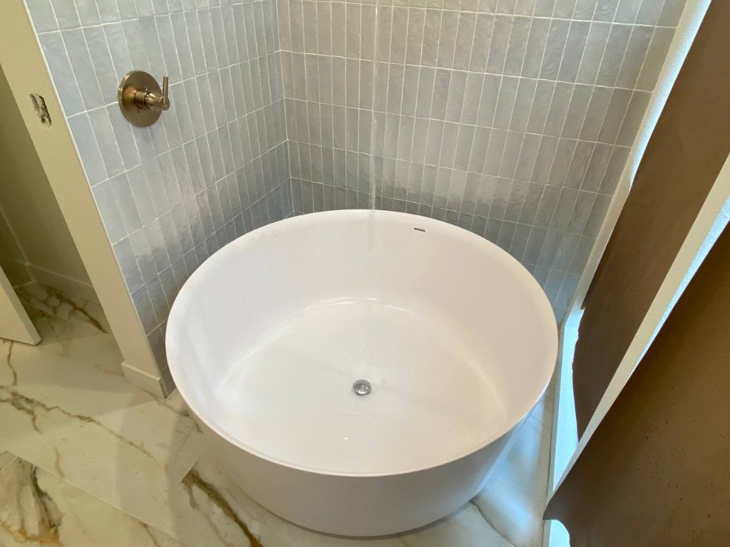 Round soaker tub against zellige tile wall