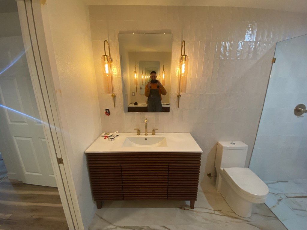 Slatted walnut vanity, brass sconces, white zellige tile — during final installation