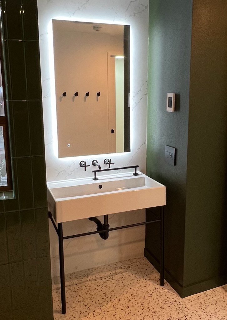 Backlit mirror, black metal console sink, wall-mount faucet, terrazzo floor