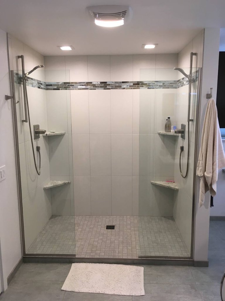 His and hers dual shower — large format white tile, glass mosaic accent band, dual hand showers and corner benches
