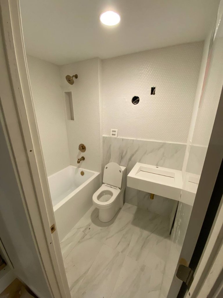 Compact bath — penny tile walls, Calacatta marble floor, floating trough sink, brass fixtures, tub with shower