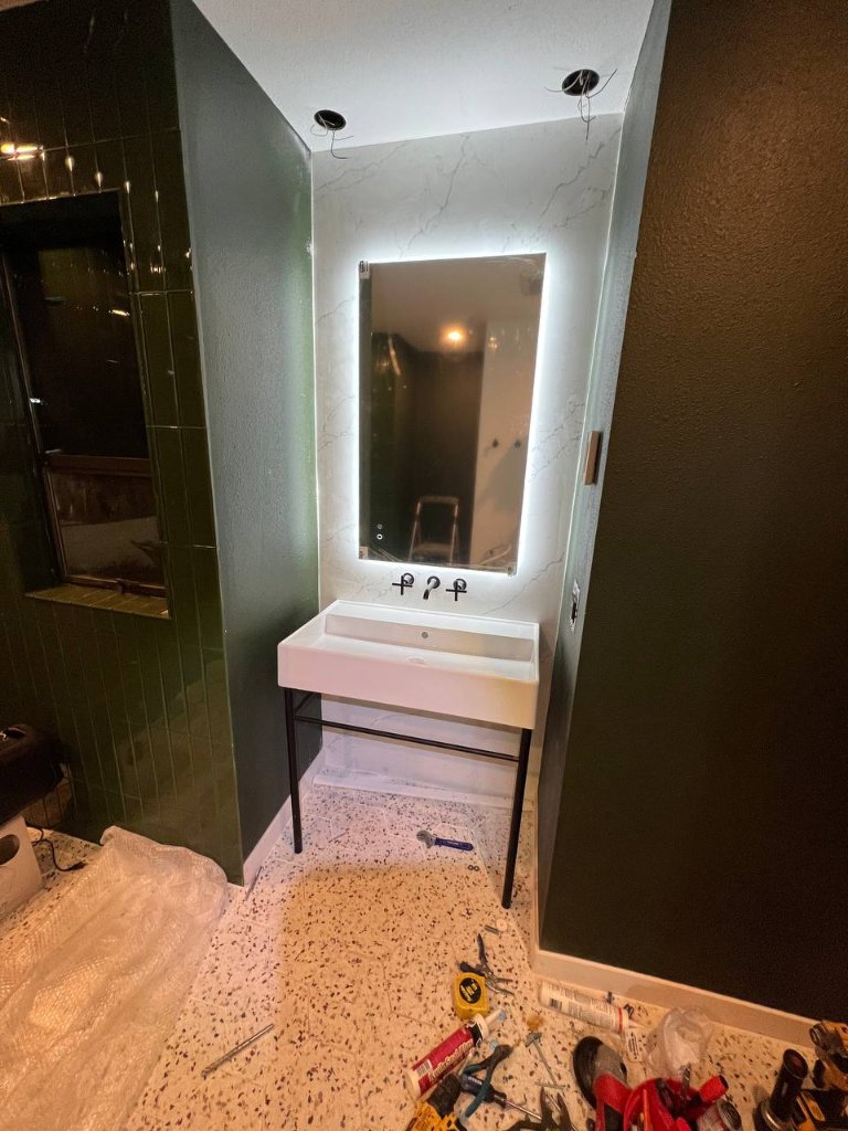 During construction — backlit mirror installed, pendant rough-ins visible in ceiling