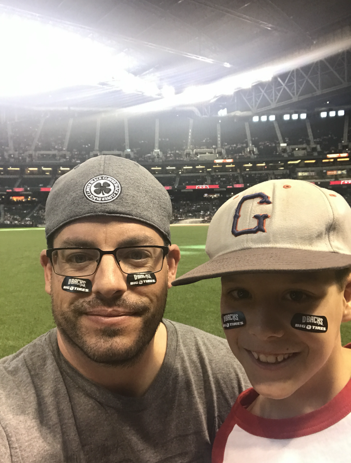 Miles Wallace and a companion wearing D-backs eye black on a baseball field at night, with the stadium visible behind them.