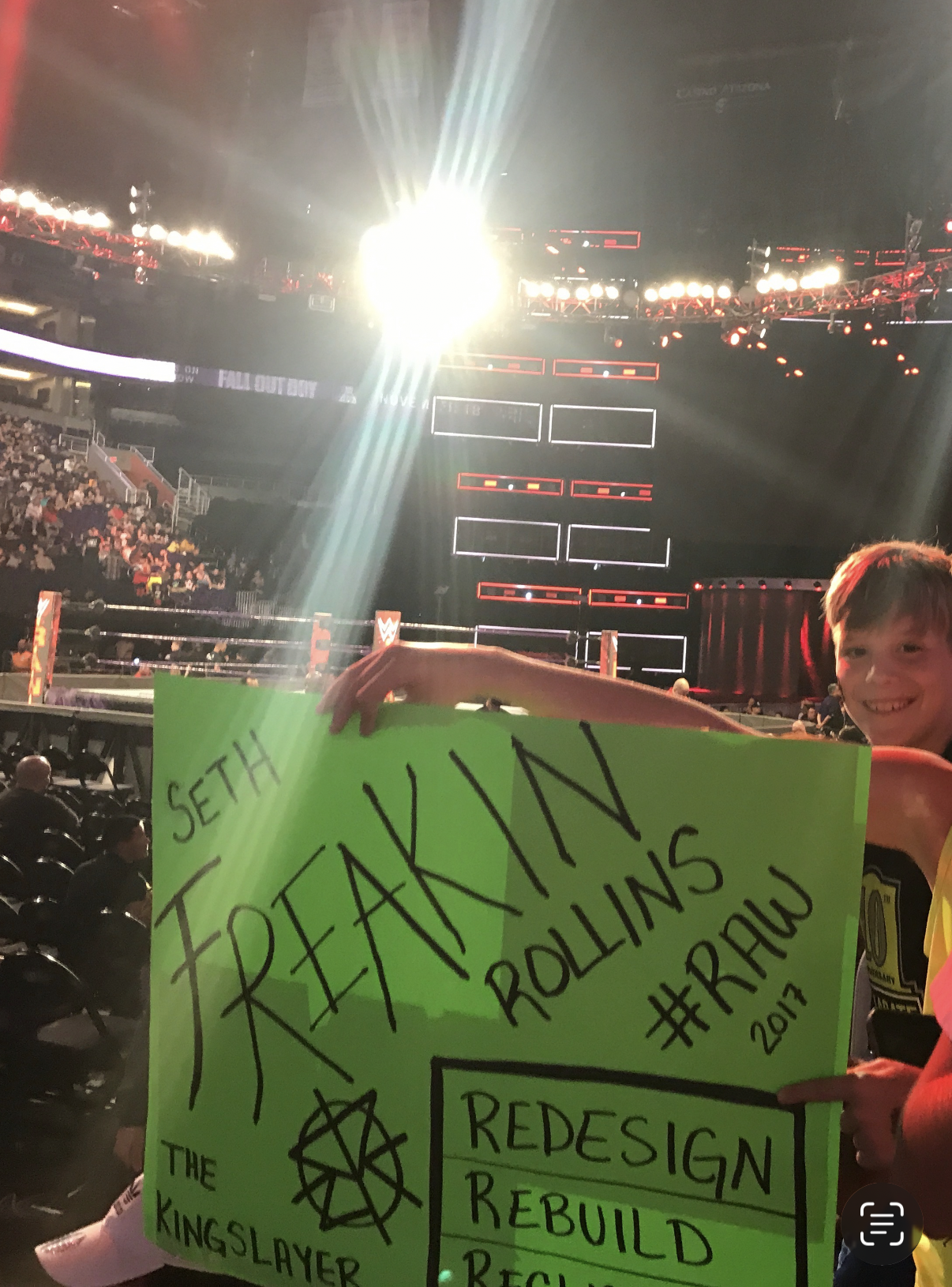 Miles Wallace holding a handmade neon-green Seth Rollins sign at WWE RAW 2017, with the arena visible behind him.