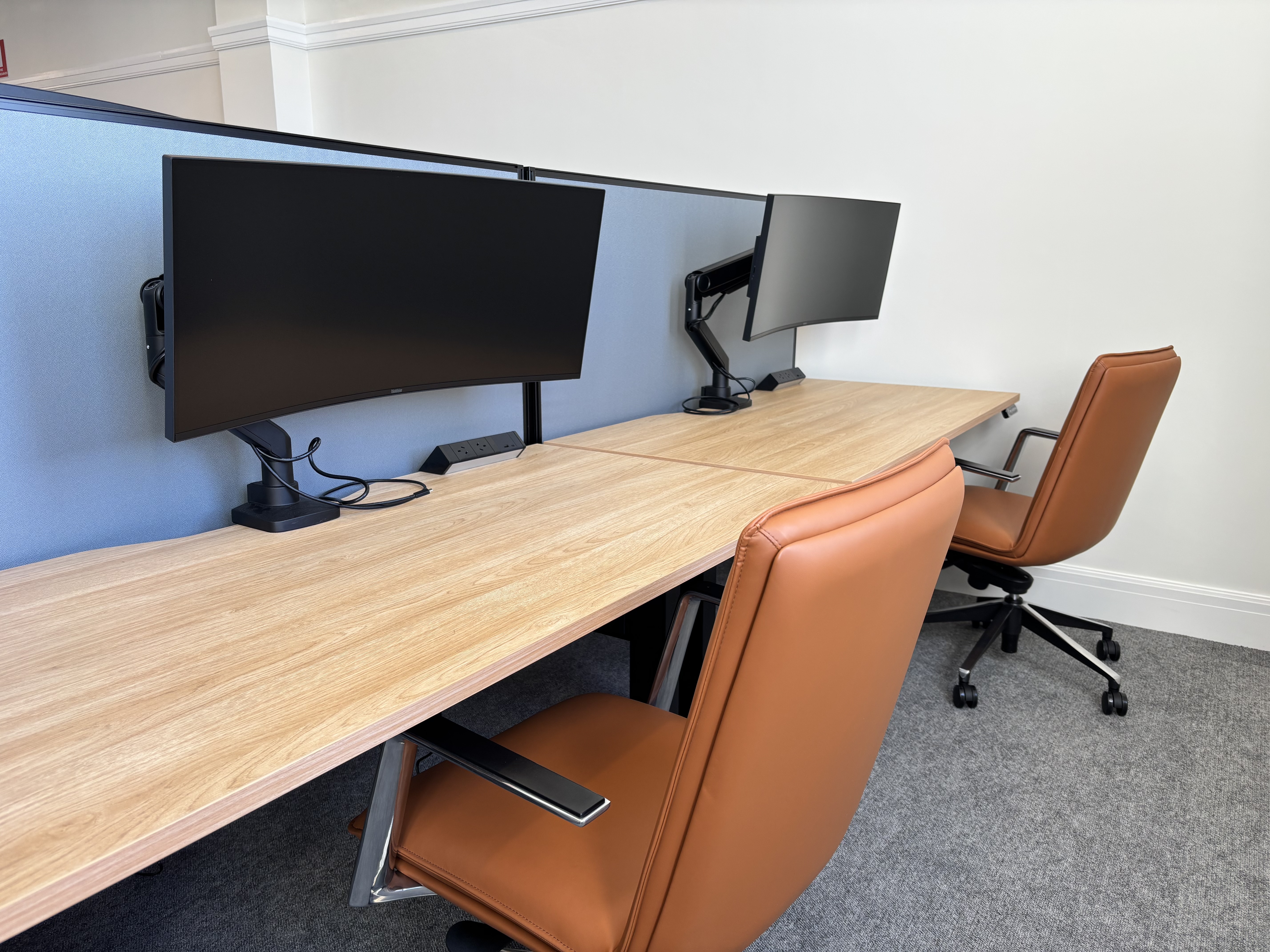 Hot desk setup with curved monitors and leather chairs