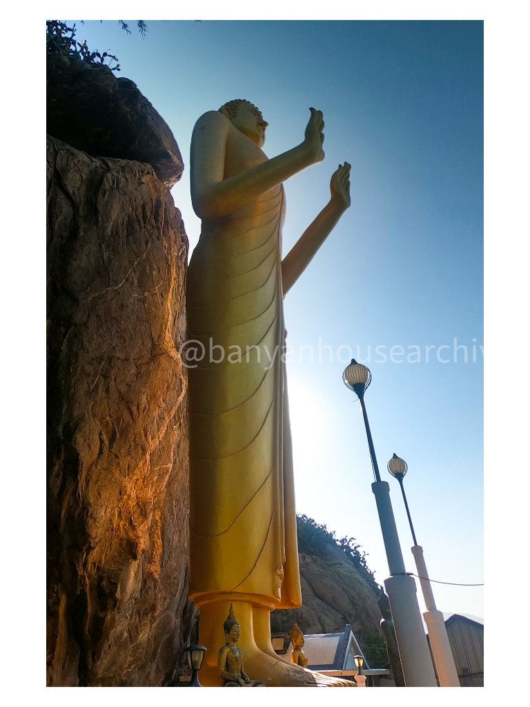 Golden standing Buddha beside a rock formation