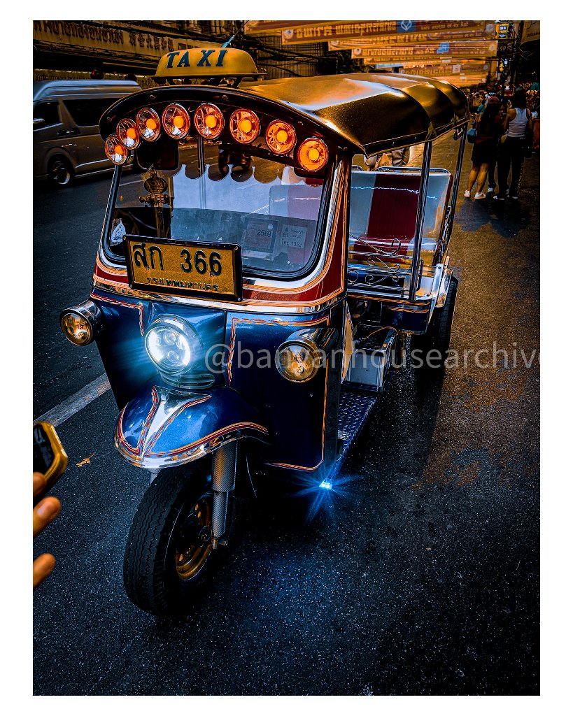 Dark blue tuk-tuk with amber roof lights at night