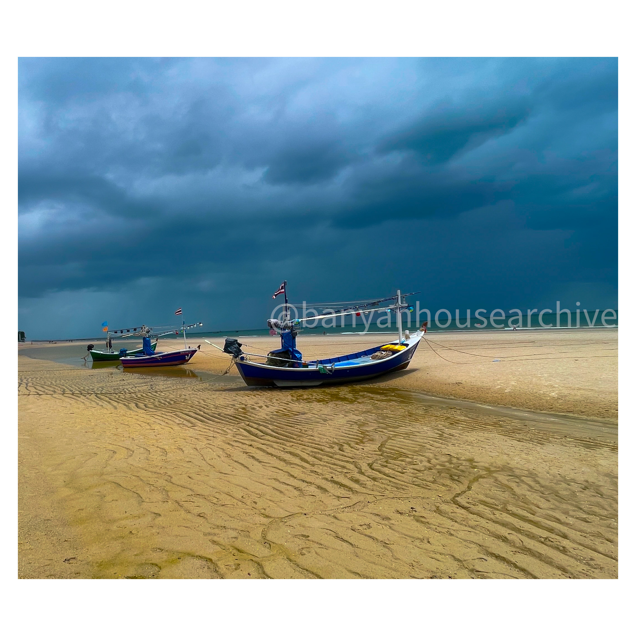 Three fishing boats beached on a shore at low tide under a stormy sky