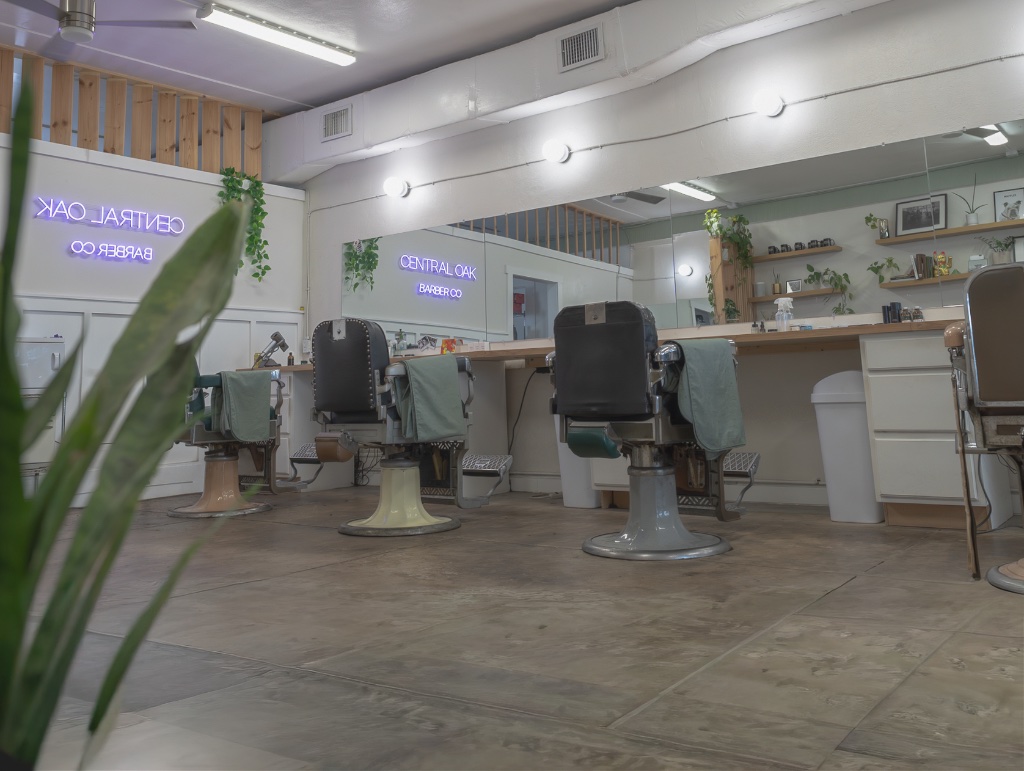 Central Oak Barber Co. interior — barber chairs, plants, and neon signage in a calm, minimalist barbershop