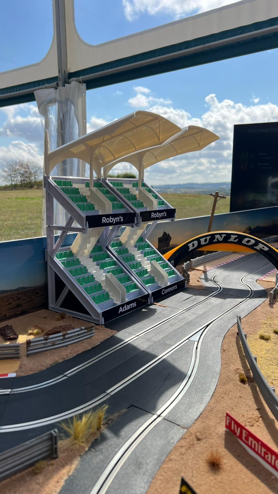 Bespoke branded grandstand with Robyn's, Adams and Connors signage alongside a Dunlop bridge on the birthday party Scalextric track