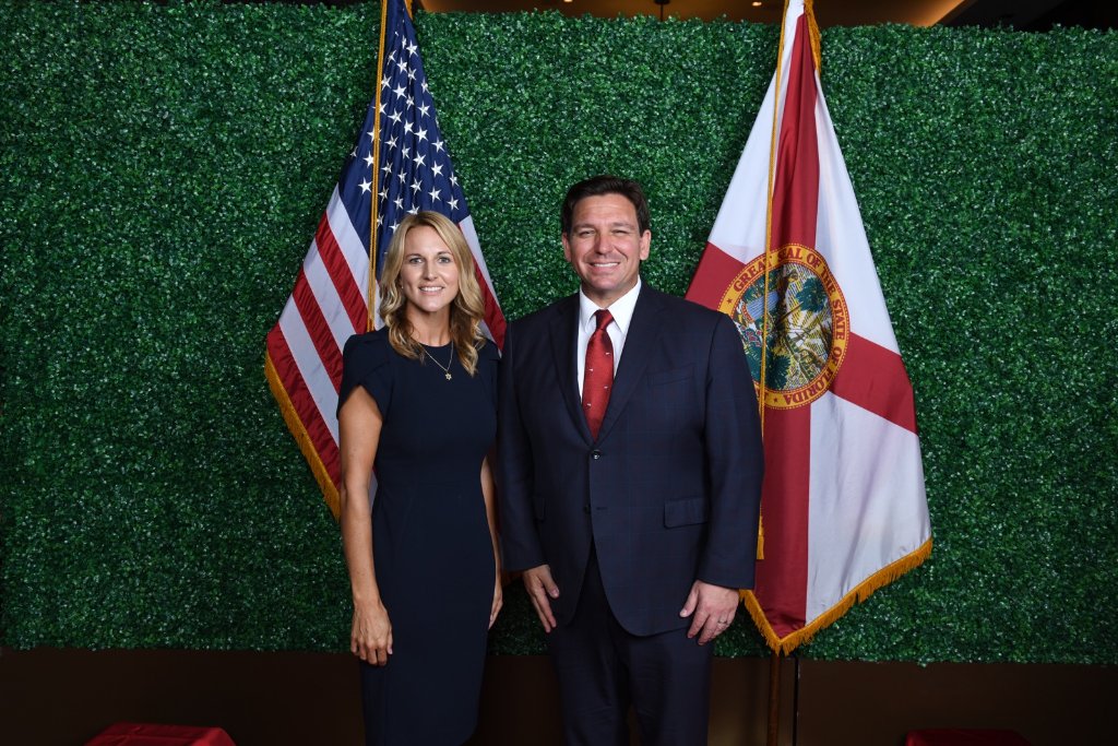 Jen Russell with Governor Ron DeSantis, standing between the United States and Florida state flags.