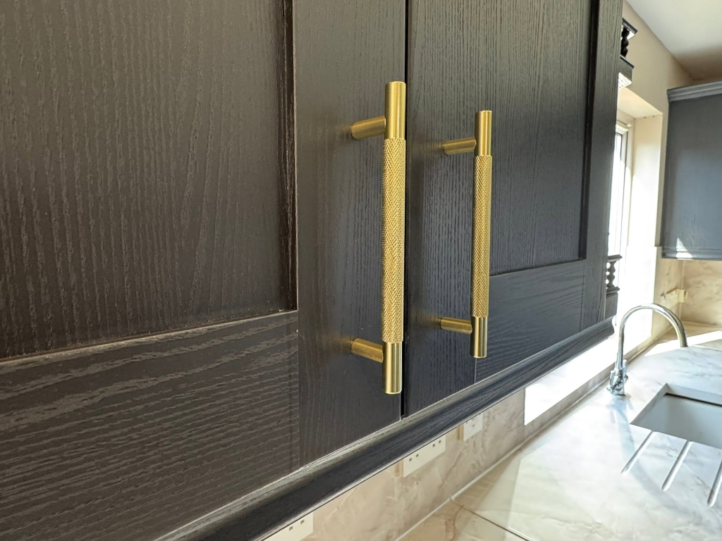 Detail of two black wood-grain cabinet doors with gold T-bar knurled handles