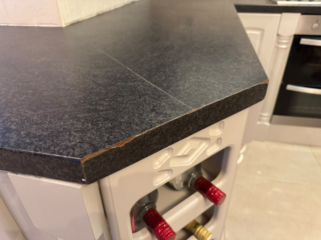 Worn and chipped dark laminate worktop corner before wrap