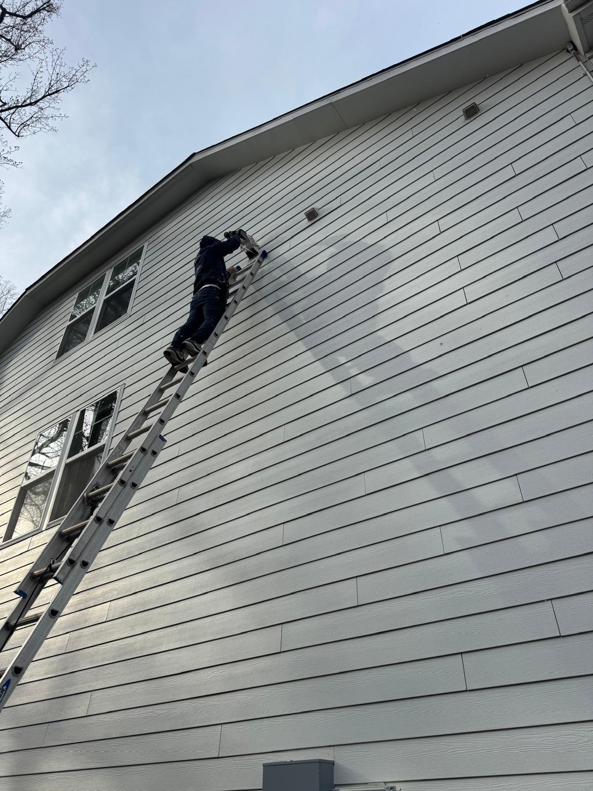 Vent guard installation on gray siding home — Fairfax County Nova technician on ladder installing vent bird guard on gray siding home — Fairfax County, VA