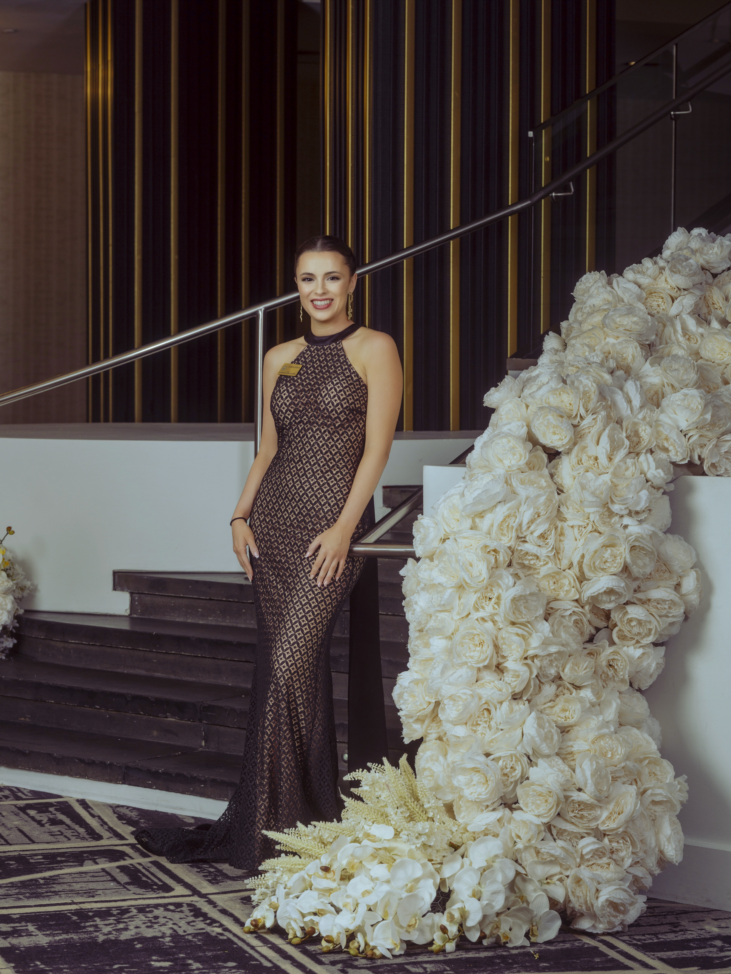 Guest in an evening gown posed beside a cascading white floral installation on a staircase