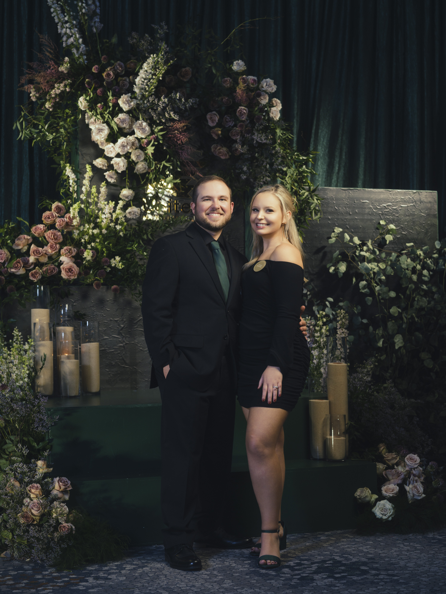 Couple standing together in a green floral portrait setting with a backdrop provided by the event design team