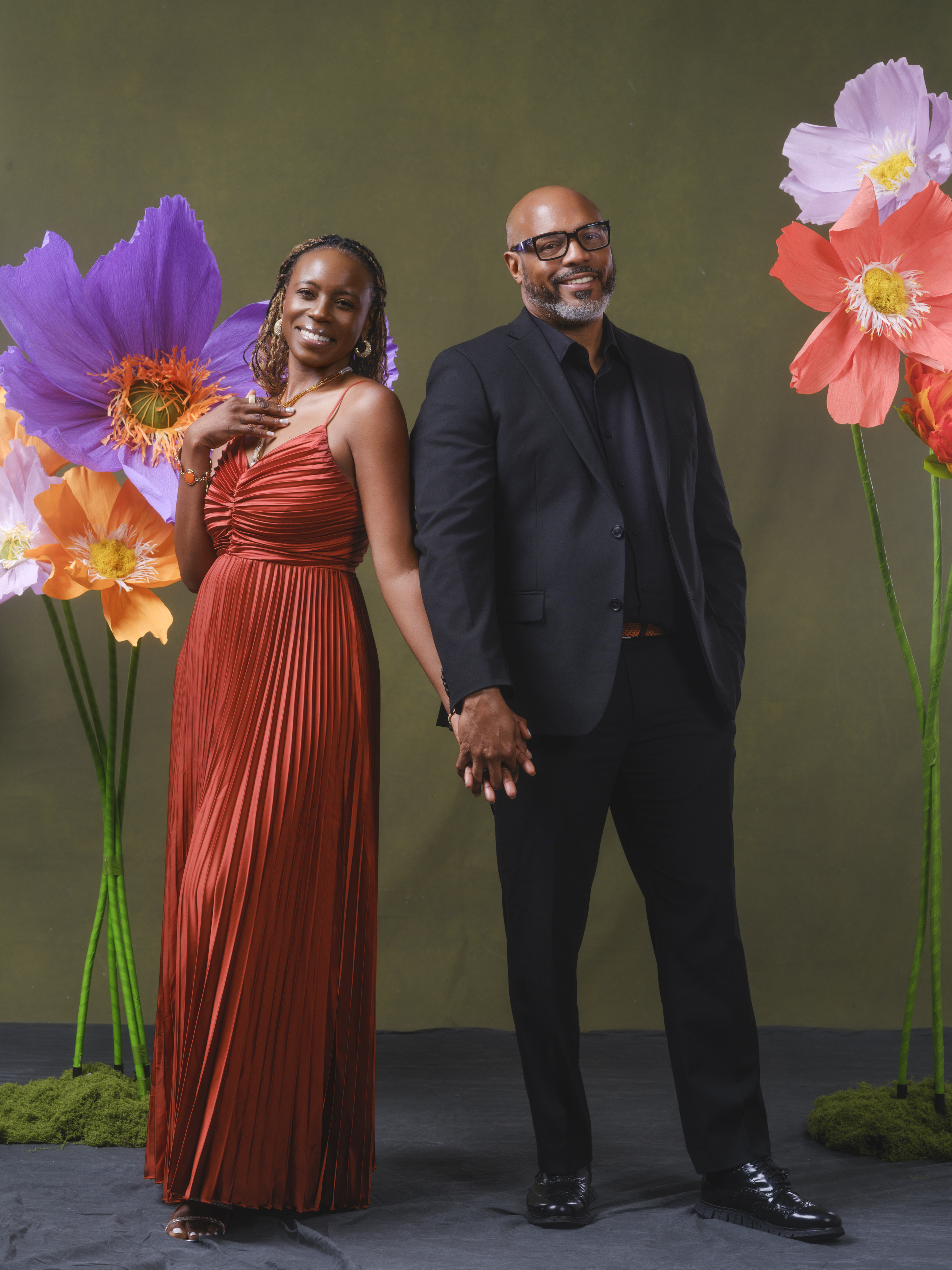 Couple holding hands within a custom portrait setting with oversized colorful flowers