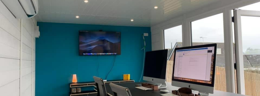 Garden office interior with desk, iMacs, and teal feature wall