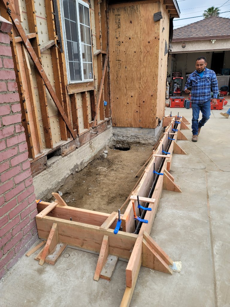 Wooden footing forms and rebar installed along side of house — room addition foundation California
