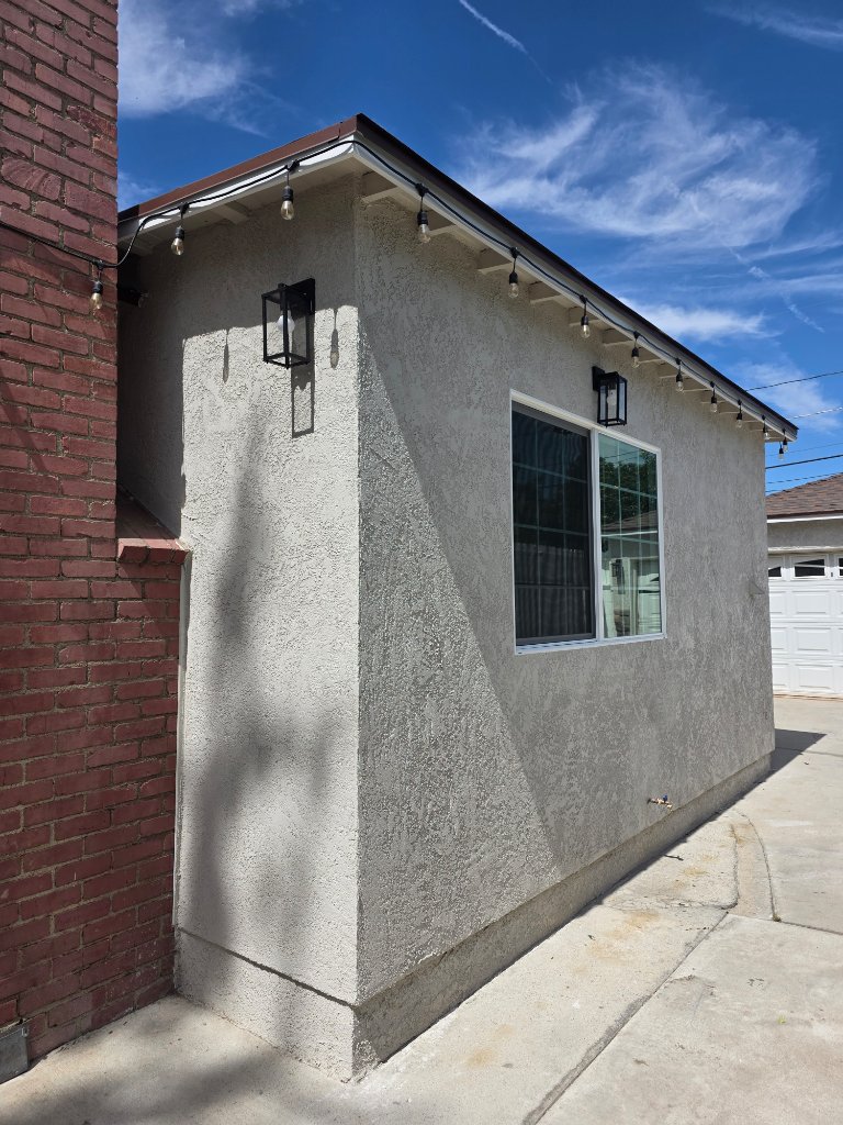 Completed stucco exterior with finished window, exterior lights, and roof eaves — finished room addition Los Angeles