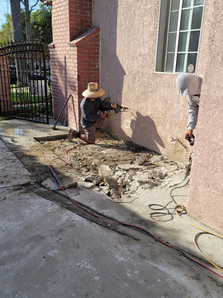Two workers breaking concrete next to pink exterior wall — demolition for room addition Los Angeles